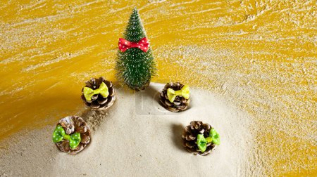 Photo for Christmas tree and pinecones with bow ties on yellow background sprinkled with white sand, creative Christmas concept - Royalty Free Image