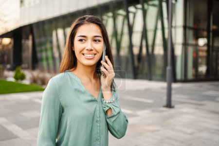 Photo for Portrait of smiling young brunette girl using mobile phone outdoors. - Royalty Free Image