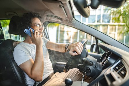 Téléchargez les photos : Homme aux cheveux bouclés et lunettes de soleil, conduit une voiture, fume une cigarette et utilise le téléphone. - en image libre de droit