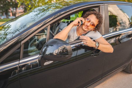 Photo for Man with curly hair and sunglasses, driving a car, smoking a cigarette, using the phone and looking in the rearview mirror. - Royalty Free Image