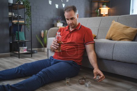 Téléchargez les photos : Mature homme assis sur le sol et boire de l'alcool. - en image libre de droit