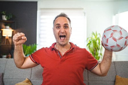 Photo for Excited middle aged man watching soccer game at home. - Royalty Free Image