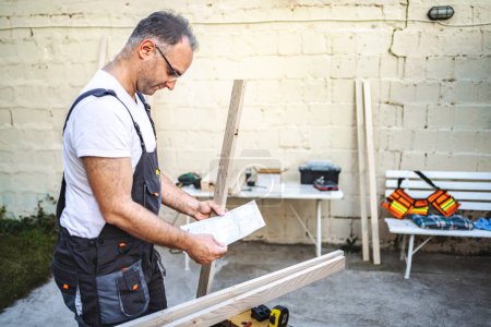 Téléchargez les photos : Mature charpentier masculin travaillant avec planche en bois à l'extérieur. - en image libre de droit