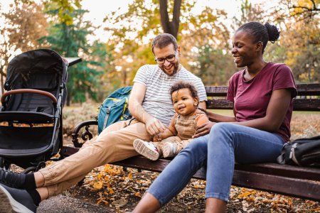 Photo for Mixed race couple is sitting on a park bench with their son. - Royalty Free Image