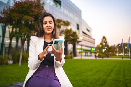 Téléchargez les photos : Achats en ligne femme d'affaires sur un téléphone portable au parc après le travail. - en image libre de droit