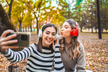 Zwei Frauen sitzen auf dem Boden und tragen Kopfhörer. Sie konzentrieren sich darauf, gemeinsam Musik oder Audio zu hören, möglicherweise ein Gespräch zu führen oder einen Podcast zu genießen..