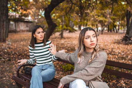 Téléchargez les photos : Deux femmes sont assises sur un banc du parc et se signalent mutuellement avec des paumes tendues qu'elles ne veulent plus les entendre et qu'elles sont en colère - en image libre de droit