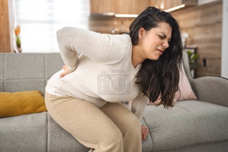 Foto de Mujer que sufre de dolor de espalda mientras está en casa. - Imagen libre de derechos