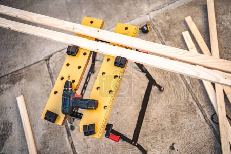 Electric drill and wooden plank on a table outdoors.