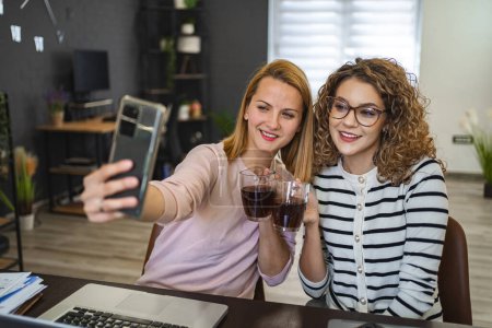 Foto de Dos compañeras están sentadas en la mesa con una taza de café y tomando una selfie. - Imagen libre de derechos