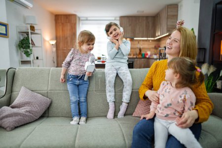 Photo for Mother and her three daughters are on the couch, having fun, singing into the microphone and having a karaoke party in the living room. - Royalty Free Image