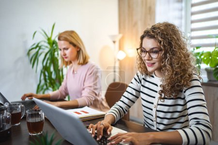 Foto de Dos mujeres están sentadas en una mesa, ambas enfocadas en la pantalla de un portátil. Aparecen comprometidos en la conversación o trabajando en colaboración en el ordenador. - Imagen libre de derechos
