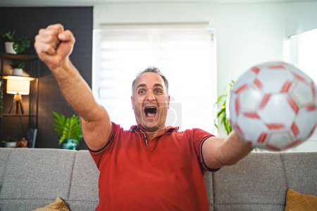 Photo for Excited middle aged man watching soccer game at home. - Royalty Free Image