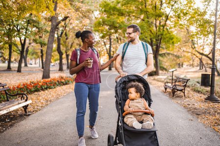 Photo for Mixed race couple walks their sons stroller through the park. - Royalty Free Image