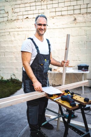 Téléchargez les photos : Mature charpentier masculin travaillant avec planche en bois à l'extérieur. - en image libre de droit