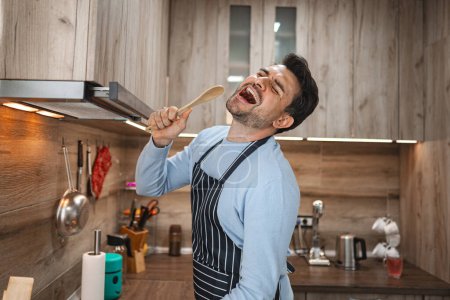 Hombre de pelo castaño canta alegremente en una estufa de madera en la cocina mientras cocina.