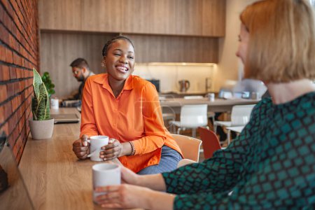 Foto de Una mujer está sentada en una mesa, sosteniendo una taza de café. Ella parece relajada, bebiendo en su bebida en un ambiente acogedor. - Imagen libre de derechos