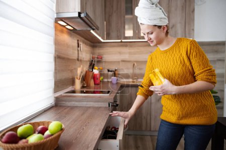 Foto de Una mujer está de pie en la cocina con una toalla en la cabeza. Se hace un café.. - Imagen libre de derechos