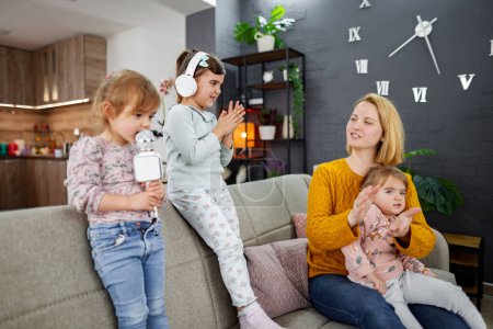 Photo for Mother and her three daughters are on the couch, having fun, singing into the microphone and having a karaoke party in the living room. - Royalty Free Image