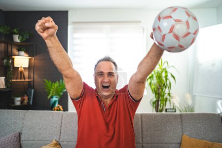 Excited middle aged man watching soccer game at home.