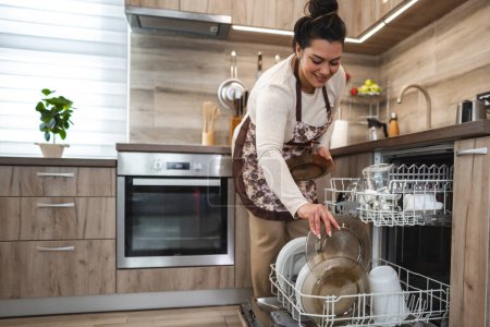 Téléchargez les photos : Femme chargeant le lave-vaisselle dans la cuisine. - en image libre de droit
