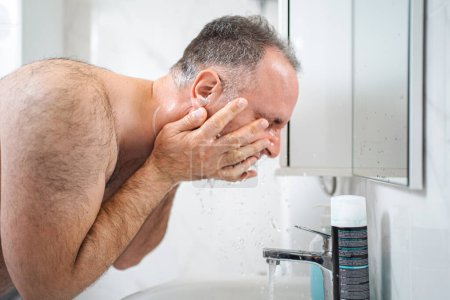 Téléchargez les photos : L'homme se lave après le rasage dans la salle de bain. - en image libre de droit