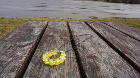 Jewelry in nature - Necklace with yellow flower beads pendant on a wooden table at a frozen lake