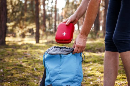 Photo for Woman taking out first aid kit from backpack. Travel insurance for all eventualities. Prepared for health problems during hiking - Royalty Free Image