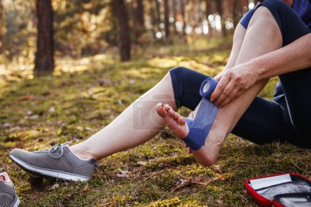Photo for Injured woman using elastic bandage for fixation sprain ankle. Health accident during hiking outdoors - Royalty Free Image