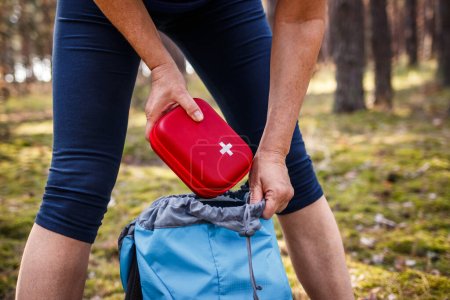 Woman taking out first aid kit from backpack. Prepared for health problems during hiking. Travel insurance for all eventualities