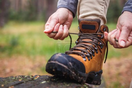 Photo for Woman tying shoelace on her hiking boot. Tourist is getting ready for hike at forest trekking trail - Royalty Free Image