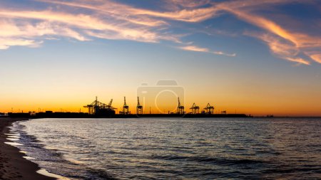 Photo for Sunset over harbor in Gdansk with commercial dock and cranes. View from Stogi beach in Baltic sea. Silhouette of industrial port - Royalty Free Image