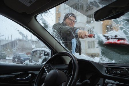 Téléchargez les photos : Homme enlève la neige de sa voiture, vue intérieure - en image libre de droit