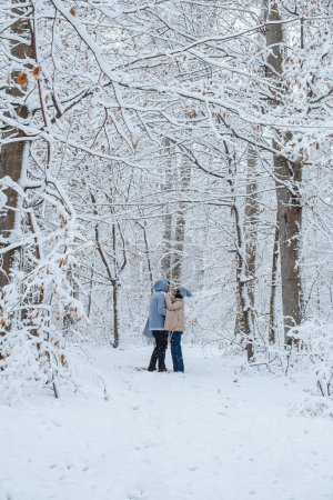 Photo for In snowy forest man circles woman in his arms as he embraces her - Royalty Free Image