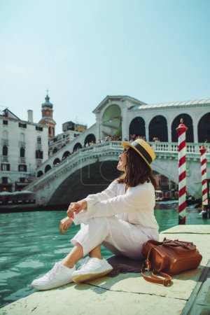 Téléchargez les photos : Femme assise près du pont rialto dans venice italie regardant grand canal avec gondoles espace de copie heure d'été - en image libre de droit