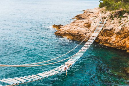 Téléchargez les photos : Homme posé au pont suspendu jouissant d'une vue sur la mer et la nature calme heure d "été - en image libre de droit