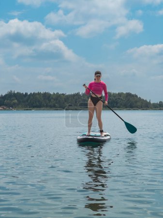 Foto de Hermosa mujer de pie en supboard mantener el equilibrio escalofriante en las actividades acuáticas del lago - Imagen libre de derechos