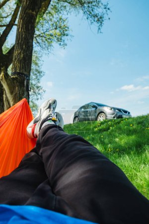 ein Mann ruht in einer Hängematte mit Blick auf ein geparktes Auto auf einem grünen Rasen in der Natur