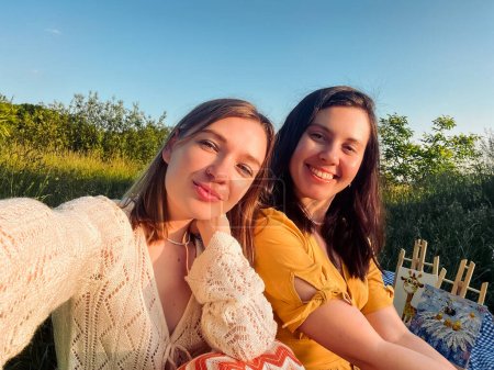 Two friends take a selfie on blue blanket for an outdoor picnic