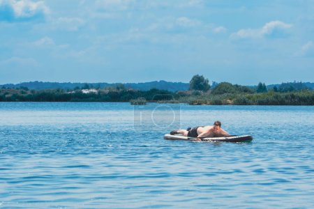 man sunbathing on supboard in the middle of the lake copy space