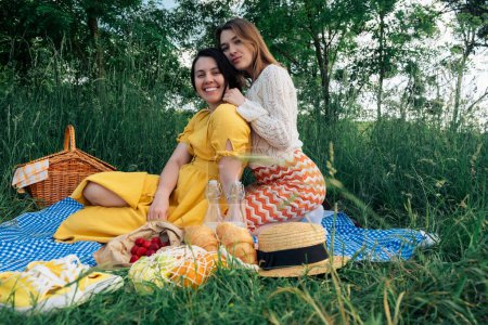 Two girls on a date sit on blue blanket for a picnic in nature