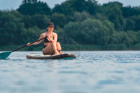 Foto de Hermosa mujer sentada en el supboard remando en el medio del lago - Imagen libre de derechos