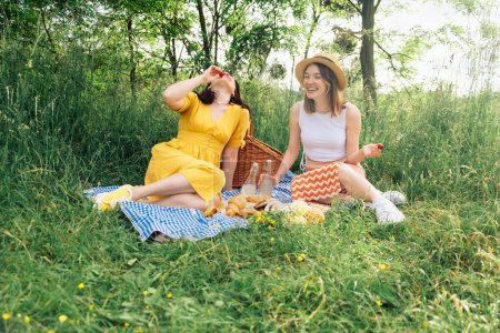 A couple of women chatting while sitting on blue picnic blanket in open air