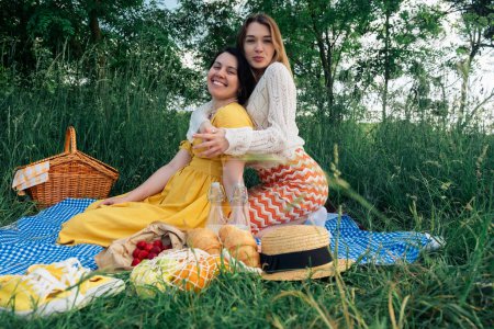 Pair of young ladies on blue blanket, having a picnic in nature.