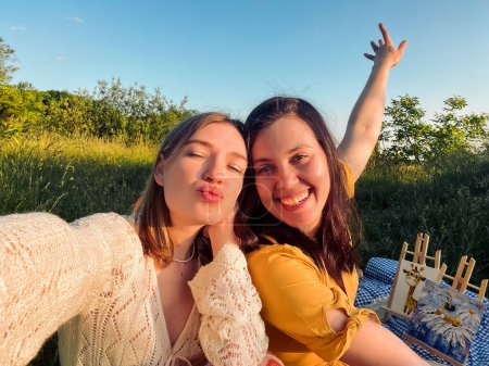 a couple of women take selfie at sunset on picnic