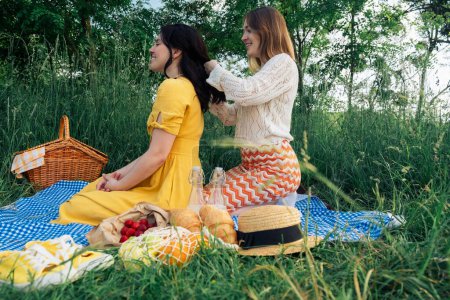 friendship: young woman styles friends hair at picnic.