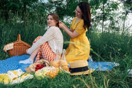 Two girls on a date sit on a blue blanket for picnic in nature