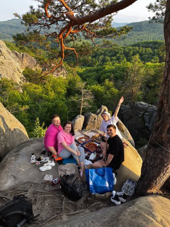 Téléchargez les photos : Amis heureux ayant pizza à la montagne falaise coucher de soleil au-dessus de la forêt - en image libre de droit