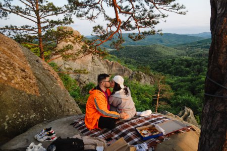 Téléchargez les photos : Couple heureux ayant rendez-vous à la falaise sur le coucher du soleil profiter du temps ensemble - en image libre de droit