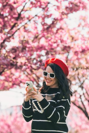 Téléchargez les photos : Portrait de belle femme souriante dans des lunettes de soleil fleur sakura sur fond - en image libre de droit